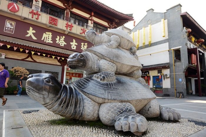 Statue of three stacked turtles in a public square in front of a curios shop.